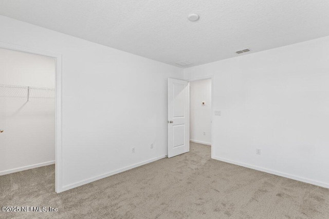 unfurnished bedroom with baseboards, a textured ceiling, a walk in closet, and carpet