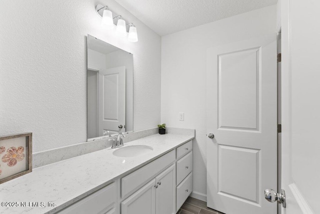 bathroom with a textured ceiling, wood finished floors, vanity, and a textured wall