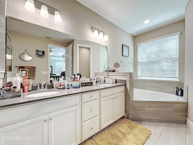 bathroom featuring a textured ceiling, double vanity, a garden tub, and a sink