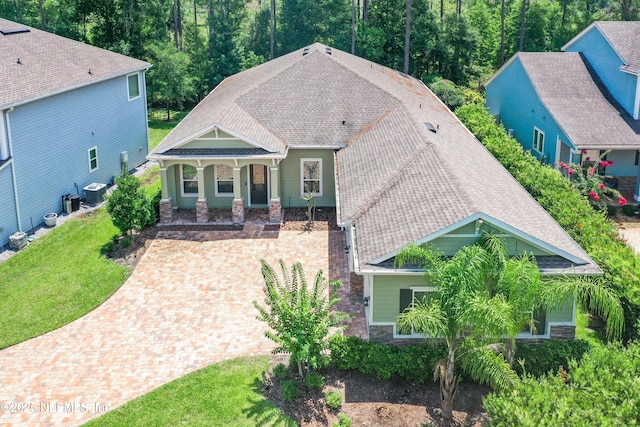 view of front of property featuring central AC, a shingled roof, a front lawn, stone siding, and decorative driveway