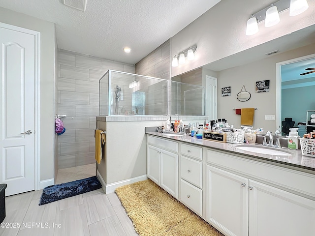 bathroom with visible vents, a sink, a textured ceiling, double vanity, and tiled shower