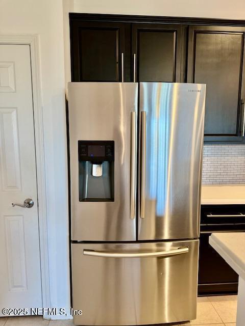 kitchen featuring light tile patterned flooring, light countertops, dark brown cabinetry, stainless steel fridge, and backsplash