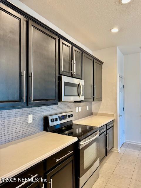 kitchen featuring backsplash, light countertops, light tile patterned floors, stainless steel appliances, and a textured ceiling