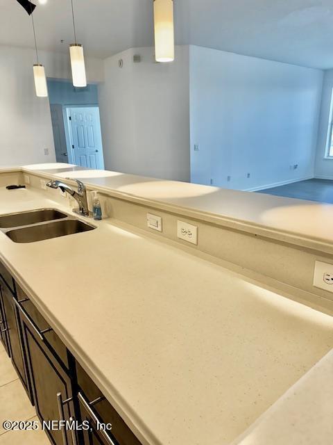 kitchen featuring light tile patterned floors, a sink, hanging light fixtures, light countertops, and dark brown cabinetry