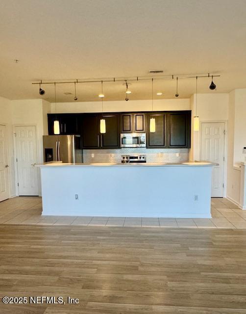 kitchen with light wood finished floors, backsplash, stainless steel appliances, and decorative light fixtures