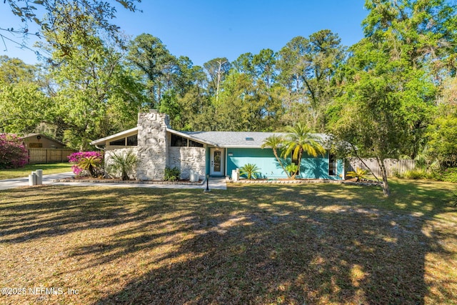 mid-century home with a chimney, a front yard, and fence