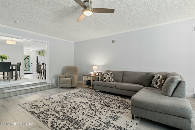 living area with ornamental molding, a ceiling fan, a textured ceiling, wood finished floors, and baseboards