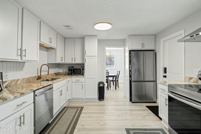 kitchen featuring light stone countertops, a sink, white cabinets, appliances with stainless steel finishes, and light wood-type flooring