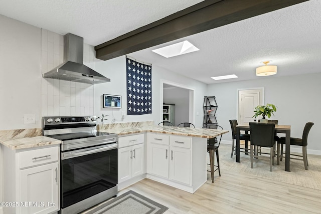 kitchen with wall chimney range hood, stainless steel electric stove, a breakfast bar, light wood-type flooring, and a peninsula