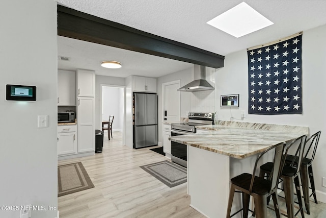 kitchen with wall chimney range hood, a kitchen breakfast bar, appliances with stainless steel finishes, a peninsula, and white cabinetry