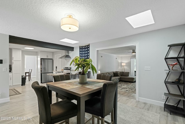 dining room featuring baseboards, light wood-style floors, a skylight, and a textured ceiling