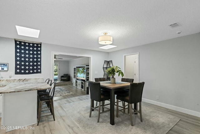 dining room with a skylight, light wood-style flooring, baseboards, and a textured ceiling