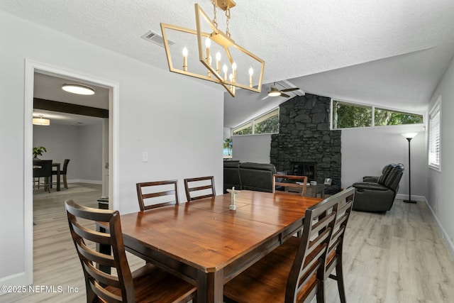 dining room with visible vents, ceiling fan with notable chandelier, wood finished floors, a fireplace, and vaulted ceiling