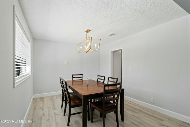 dining area with light wood-type flooring, visible vents, a notable chandelier, a textured ceiling, and baseboards