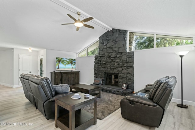 living area featuring lofted ceiling with beams, a stone fireplace, light wood finished floors, baseboards, and ceiling fan