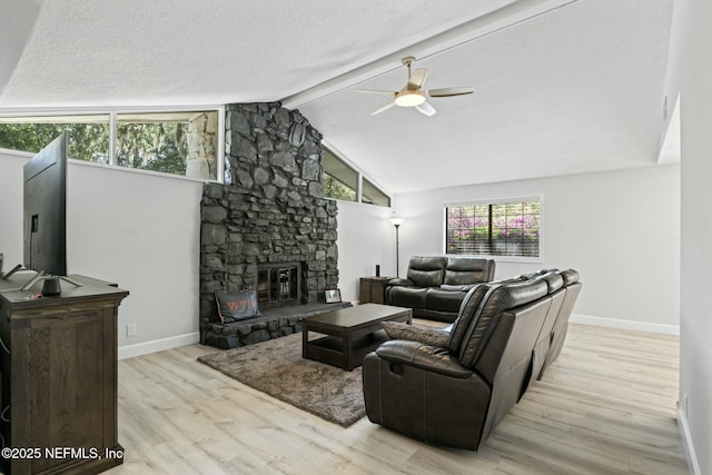 living area with ceiling fan, beam ceiling, a stone fireplace, wood finished floors, and a textured ceiling