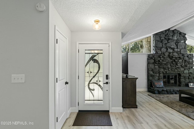 entryway with baseboards, a textured ceiling, a stone fireplace, and wood finished floors