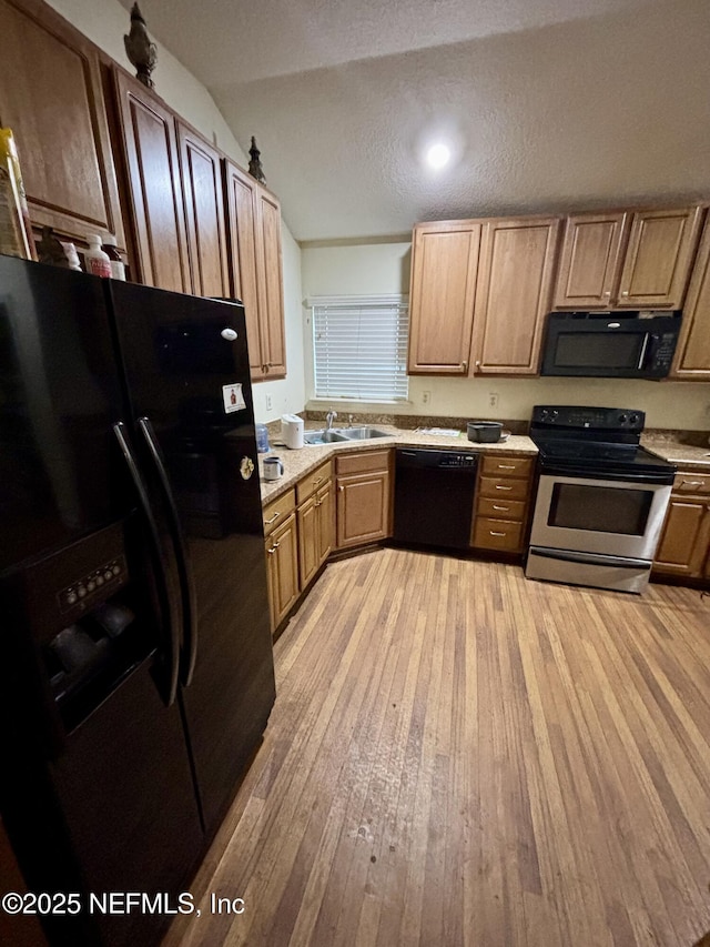 kitchen with light countertops, vaulted ceiling, light wood-style floors, black appliances, and a sink