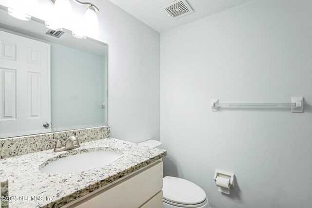 half bathroom with vanity, toilet, and visible vents