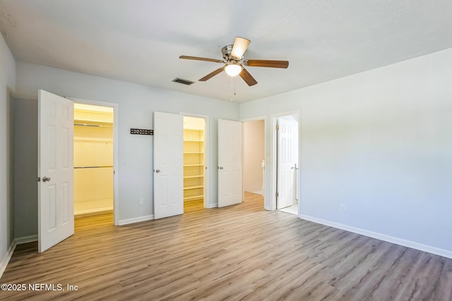 unfurnished bedroom featuring a spacious closet, wood finished floors, visible vents, and baseboards