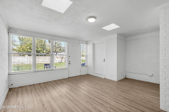 unfurnished room featuring a skylight, plenty of natural light, wood finished floors, and brick wall