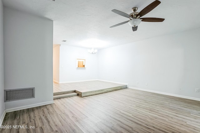 spare room featuring wood finished floors, visible vents, baseboards, a textured ceiling, and ceiling fan with notable chandelier