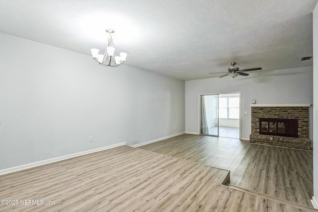 unfurnished living room featuring visible vents, a textured ceiling, wood finished floors, baseboards, and a brick fireplace