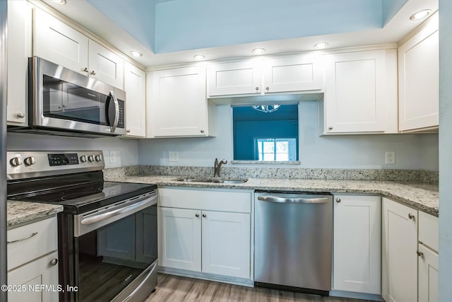 kitchen with light stone counters, light wood-style flooring, a sink, appliances with stainless steel finishes, and white cabinetry