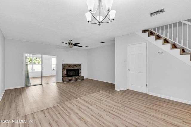 unfurnished living room featuring visible vents, ceiling fan with notable chandelier, wood finished floors, a fireplace, and stairs