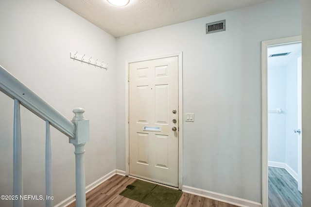 entryway with stairs, wood finished floors, visible vents, and baseboards