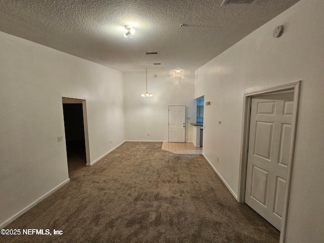 carpeted spare room with baseboards, visible vents, a textured ceiling, and an inviting chandelier