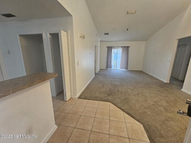 hallway with light carpet, visible vents, baseboards, and light tile patterned flooring