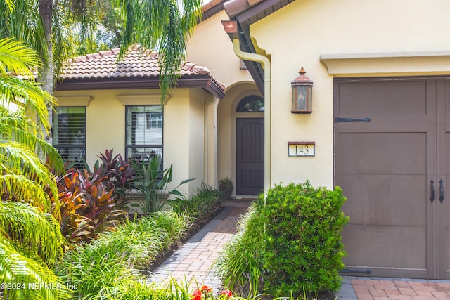 view of exterior entry with stucco siding, a tiled roof, and a garage