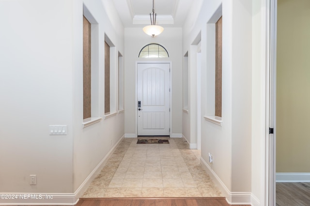 doorway with a tray ceiling, baseboards, and ornamental molding