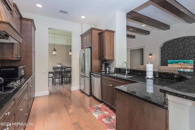 kitchen featuring visible vents, a sink, stainless steel appliances, dark stone counters, and light wood-style floors