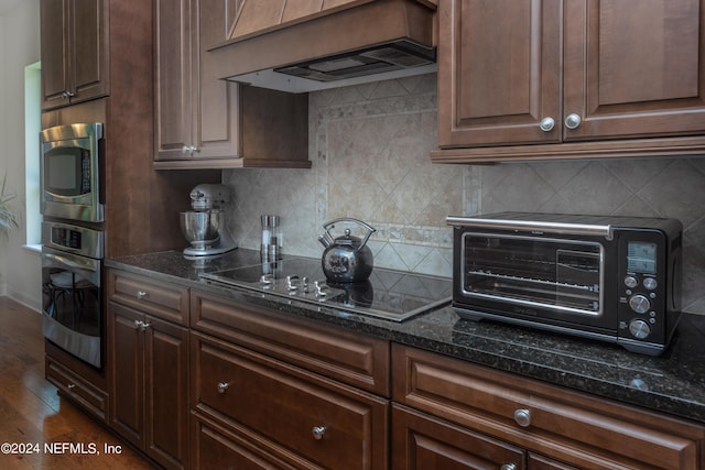 kitchen featuring custom exhaust hood, dark stone counters, a toaster, appliances with stainless steel finishes, and backsplash