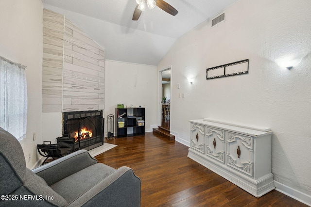 living area with wood finished floors, a ceiling fan, visible vents, a tile fireplace, and vaulted ceiling