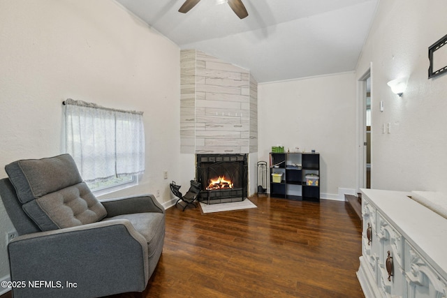 living area with a ceiling fan, a tile fireplace, wood finished floors, baseboards, and vaulted ceiling