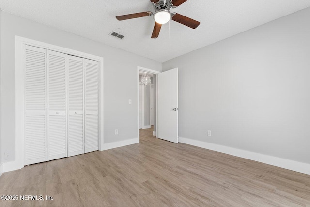 unfurnished bedroom featuring visible vents, a textured ceiling, wood finished floors, a closet, and baseboards