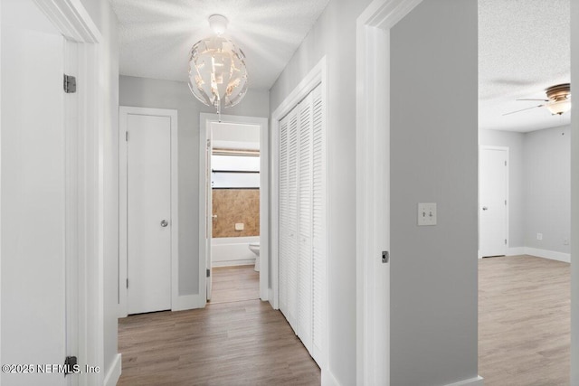 hall featuring a textured ceiling, an inviting chandelier, and wood finished floors