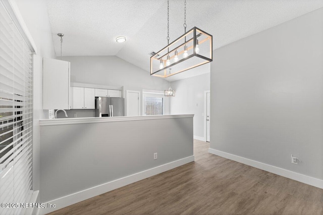 interior space with baseboards, a textured ceiling, wood finished floors, and vaulted ceiling