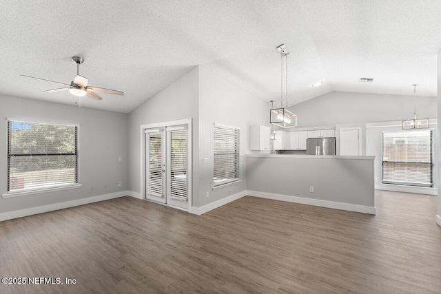 unfurnished living room featuring wood finished floors, visible vents, lofted ceiling, a textured ceiling, and ceiling fan with notable chandelier