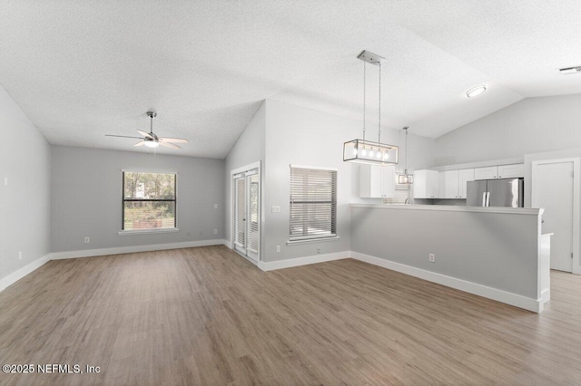 interior space with a textured ceiling, light wood-style floors, ceiling fan, and vaulted ceiling