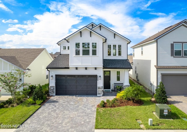 view of front of house with driveway, stone siding, a shingled roof, a front yard, and an attached garage