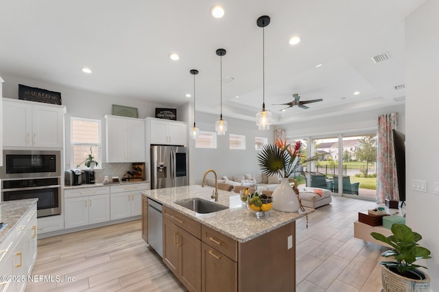 kitchen featuring backsplash, ceiling fan, open floor plan, appliances with stainless steel finishes, and a sink