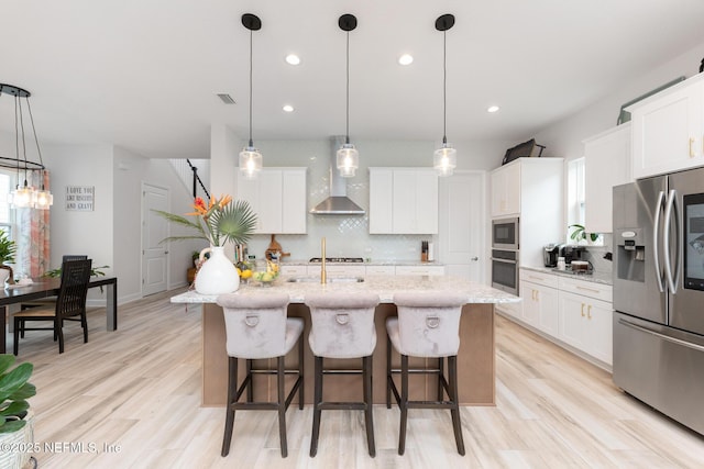 kitchen with backsplash, wall chimney exhaust hood, a healthy amount of sunlight, and appliances with stainless steel finishes