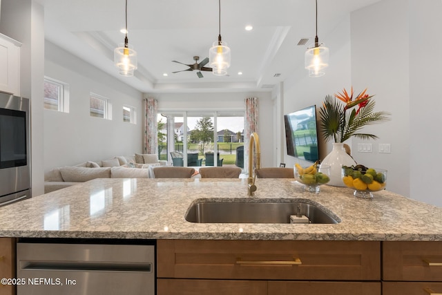 kitchen with light stone counters, a tray ceiling, ceiling fan, a sink, and open floor plan