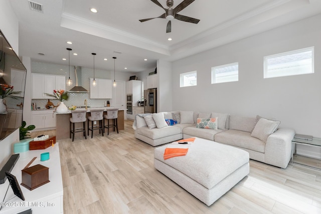 living room with visible vents, light wood-type flooring, a raised ceiling, and a ceiling fan