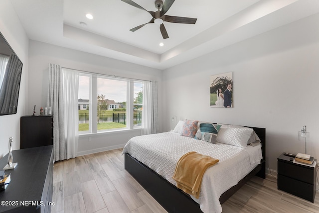 bedroom with a ceiling fan, baseboards, light wood finished floors, a tray ceiling, and recessed lighting