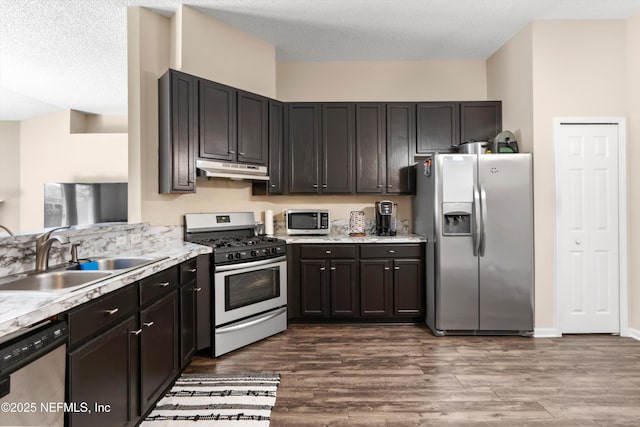 kitchen with dark wood finished floors, under cabinet range hood, appliances with stainless steel finishes, and a sink
